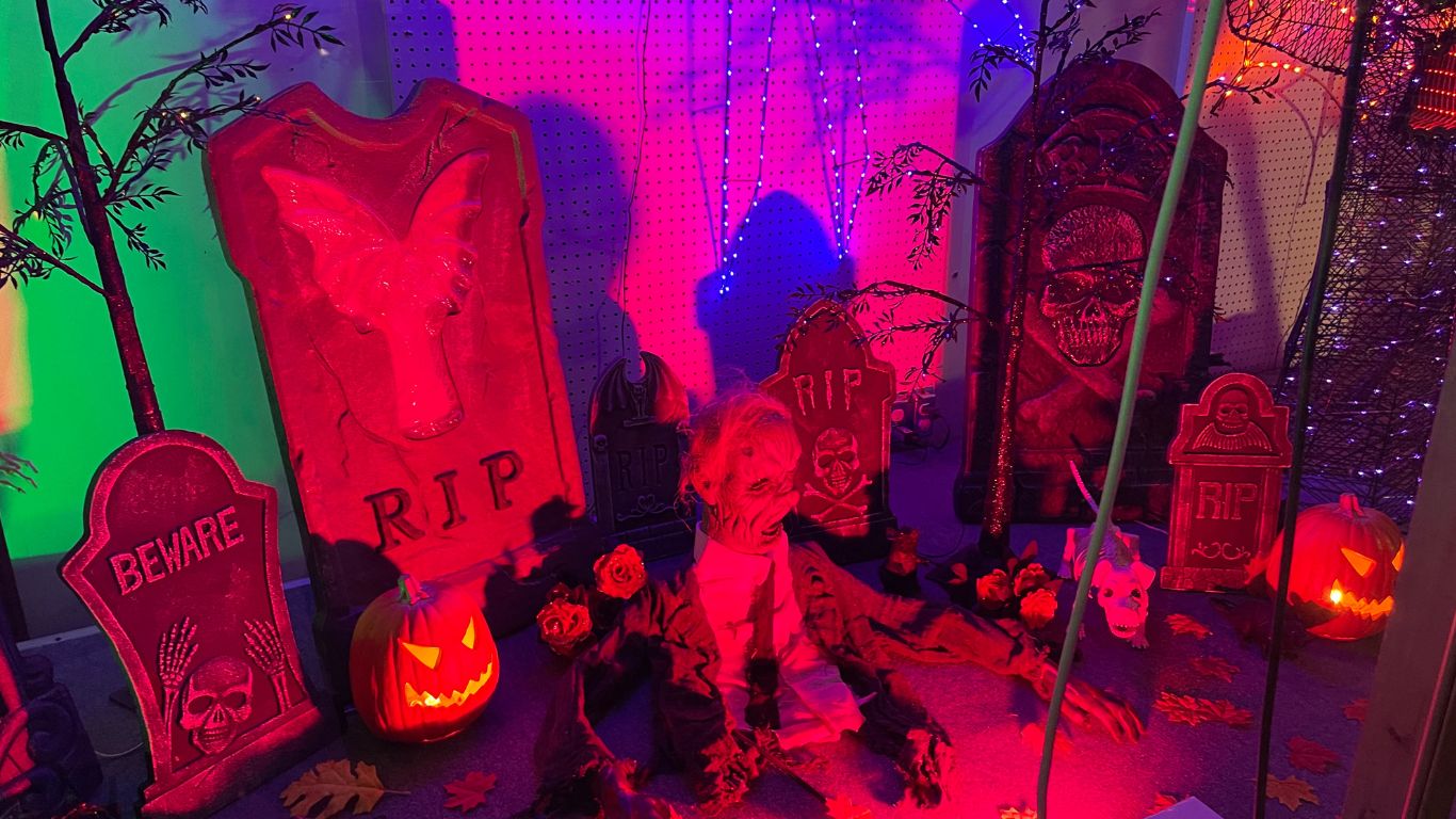 a person in a garment sitting on the ground next to a pumpkin and tombstones
